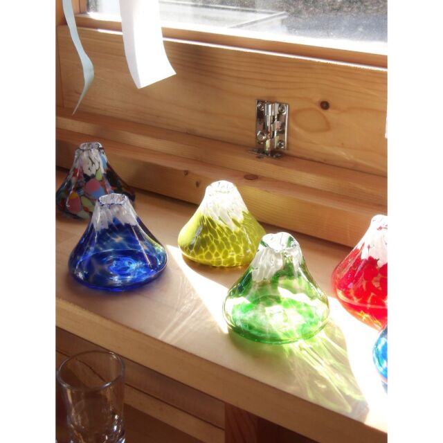 ギャラリー小屋に並べてある富士山の一輪挿し🗻
光が差すと意外な表情が見られることもあります。

ガラスの色粒の間から透けて見える光が面白いですね。

#shiraishiglassstudio 
#白石ガラス工房 
#glassflowervase 
#富士山